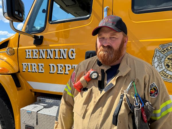 A firefighter poses for a photo next to a dark yellow truck.
