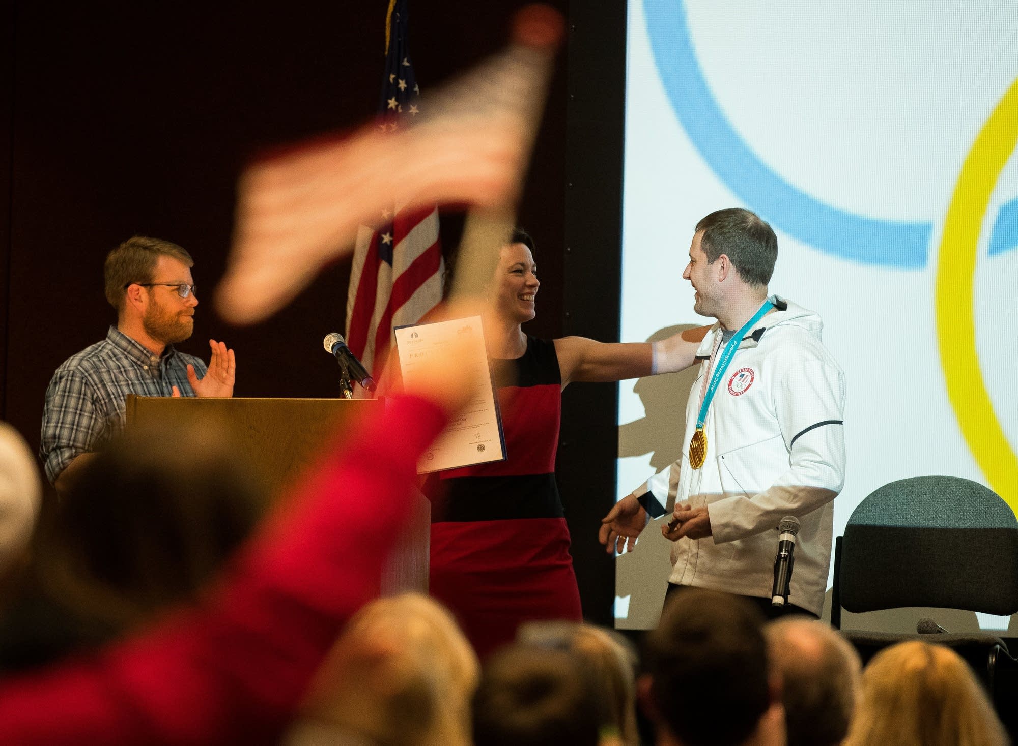 Mayors Jim Paine, left, and Emily Larson congratulate John Shuster.