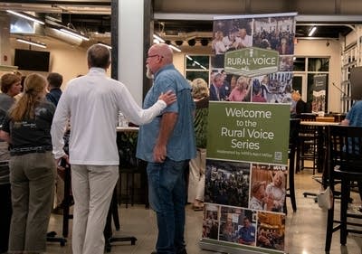 Two people stand near a sign that reads "Welcome to the Rural Voice Series."