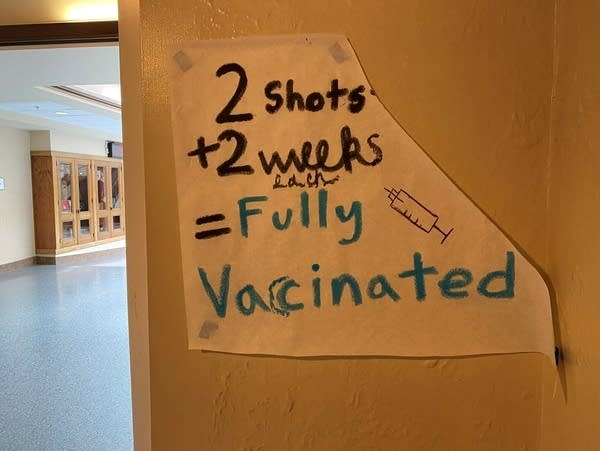 A paper sign taped to a wall says "2 shots + 2 weeks = fully vaccinated."