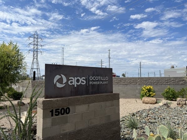 A sign for an Arizona Public Service power plant. In the background are power lines.