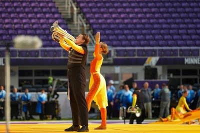 A marching band performs on the field of a football stadium.