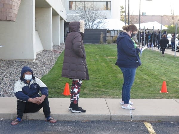 Cones and people line up in a parking lot outside of a building.