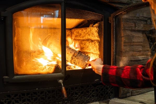 A person places a log in a fireplace