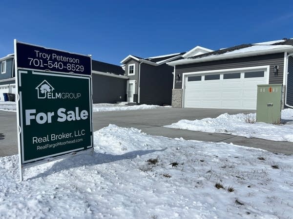 A for sale sign stands in a snowy yard.