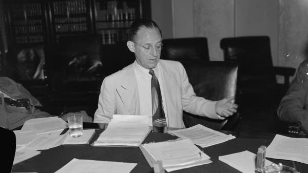A black and white photo of a man in a suit at a table.
