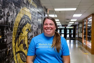 A woman in a blue shirt poses for a photo in a school hallway.