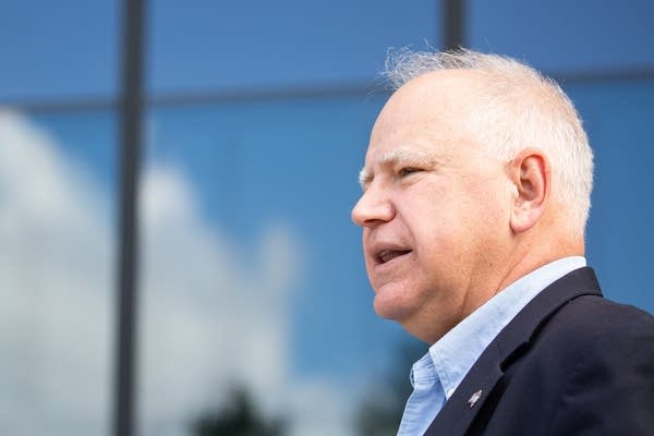 A man speaks in front of blue sky reflected in a building.