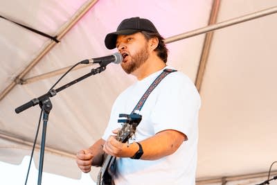 A musician sings and plays guitar on an outdoor stage