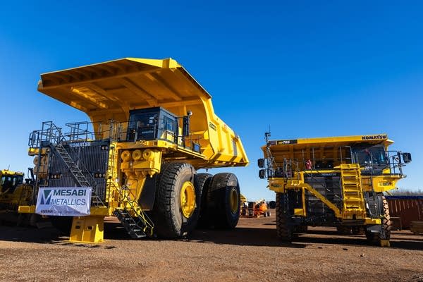 Two large, yellow construction trucks side by side. The one on the left is nearly double the height of the other.