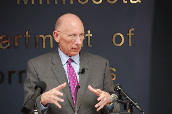 man in gray suit and pink tie talks at lectern
