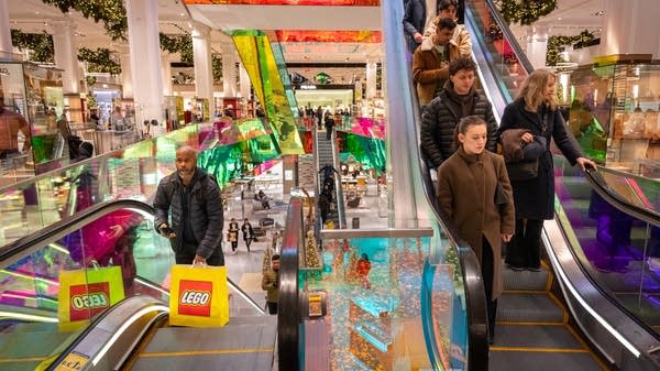 Shoppers stand on escalators at a Saks, surrounded by Christmas decorations
