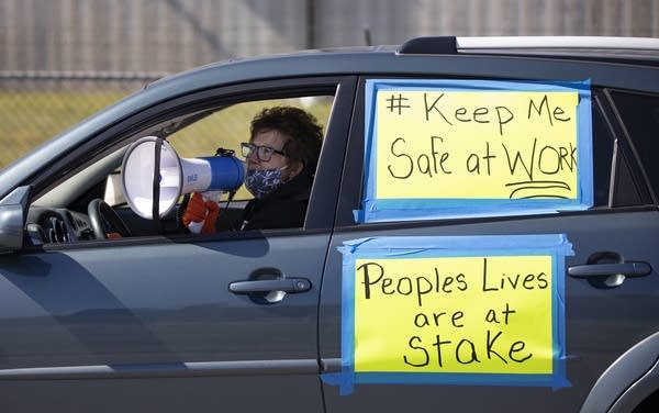 A person wearing a face mask in a car uses a megaphone. 