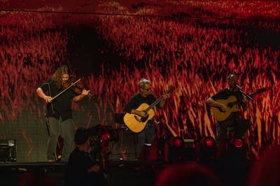 Three musicians performing on a large outdoor stage