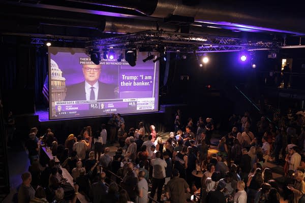 Political supporters watch election results come in on large screens at a concert venue.