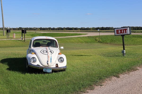 A white Volkswagen Beetle with red and blue stripes sits in a patch of grass.