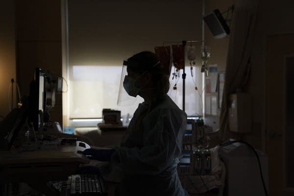 A nurse works on a computer in a hospital room.