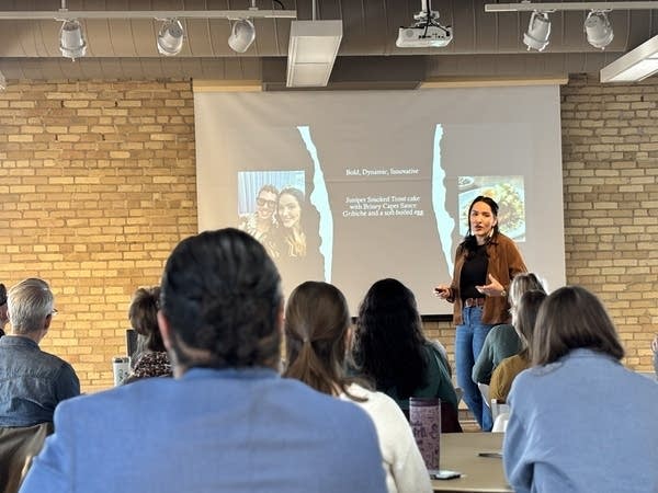 A woman speaks in front of a powerpoint