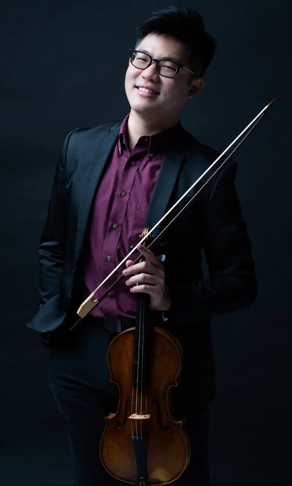 Violinist Alan Choo poses with his violin in a suite and purple shirt