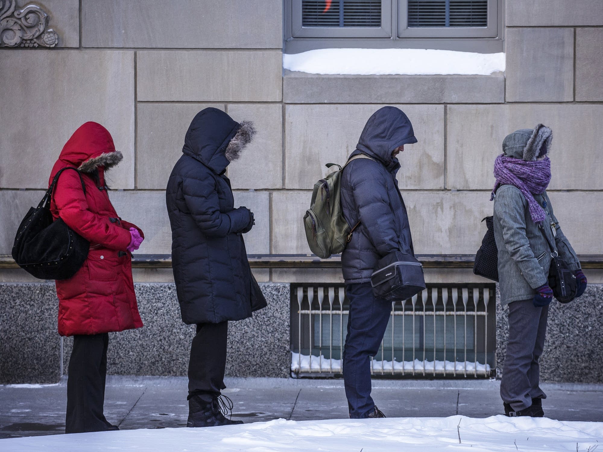 People bundled up in their hooded jackets wait for a a bus in Rochester.