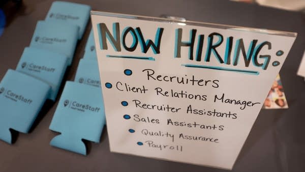 SUNRISE, FLORIDA - JUNE 23: A 'Now Hiring' sign is seen on the CareStaff company table setup at the Mega Job Fair held at the FLA Live Arena on June 23, 2022 in Sunrise, Florida. The job fair had 8,000 jobs available from 100 different employers and expected approximately 3000 people to attend the fair.