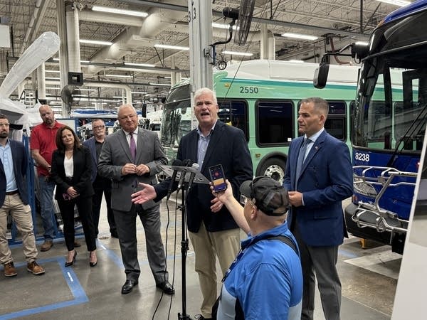 A group in a manufacturing warehouse, one man speaks.