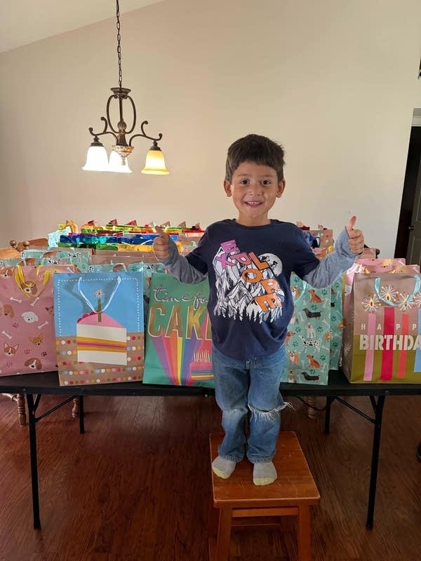 Boy thumbs up in front of many gift bags