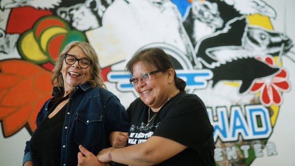 Two people laugh while standing in front of a mural.