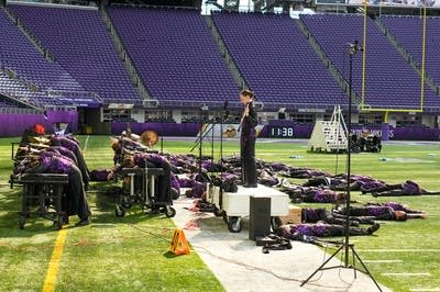 A marching band performs on the field of a football stadium.