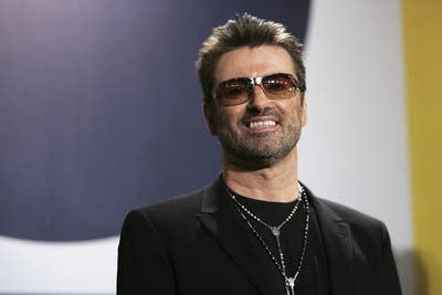 A man in sunglasses smiles for photographers