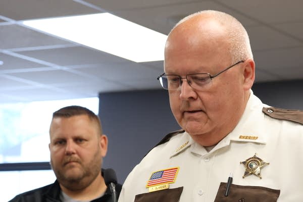 A sheriff looks down while giving a press conference. Another man stands beside him.