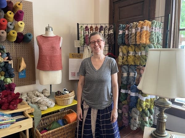 A middle aged woman poses in front of a display of colorful yarn