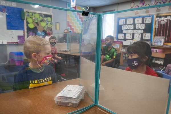 Two students look are separated by a plastic barrier. 