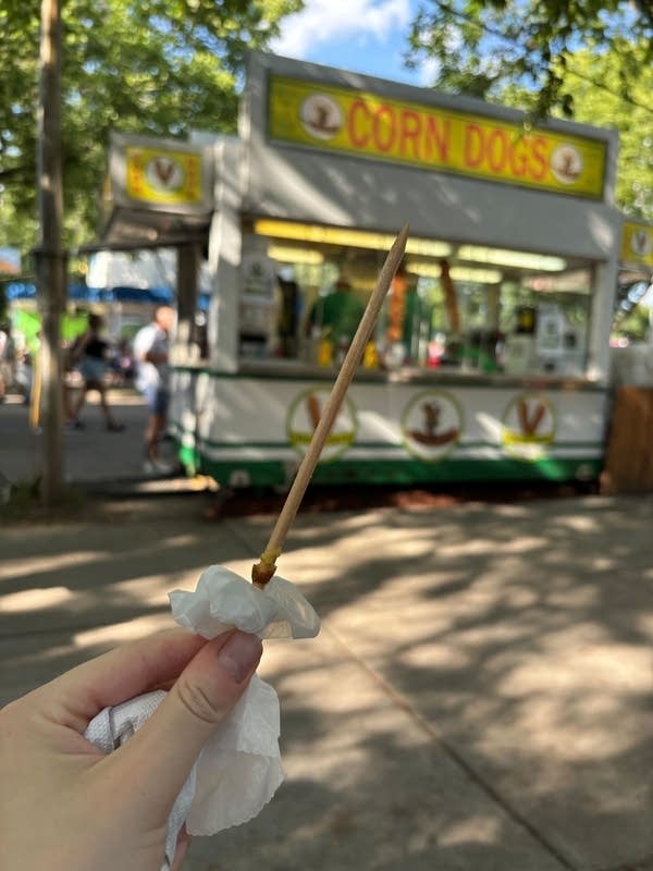 Close-up of an empty corn dog stick, with the corn dog stand in the background.
