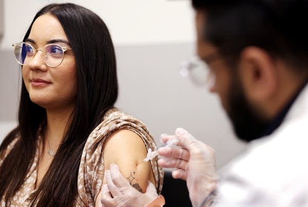 A woman with glasses receives a shot in her shoulder.