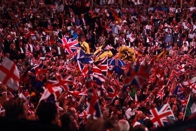 A large music venue filled with people cheering and waving flags