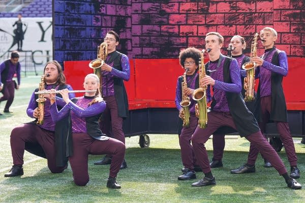 A marching band performs on the field of a football stadium.