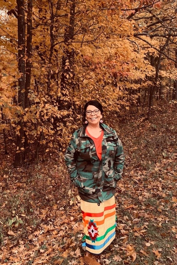 A woman poses for a photo in front of fall foliage.