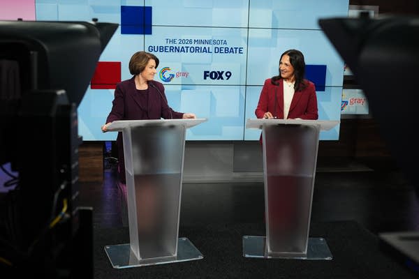 two women stand at podiums during a debate