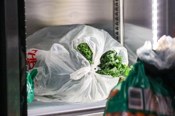 A plastic bag of greens is seen in a refrigerator.