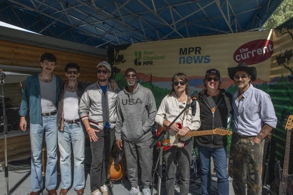 Seven people pose for a photo together on an outdoor stage at a fair
