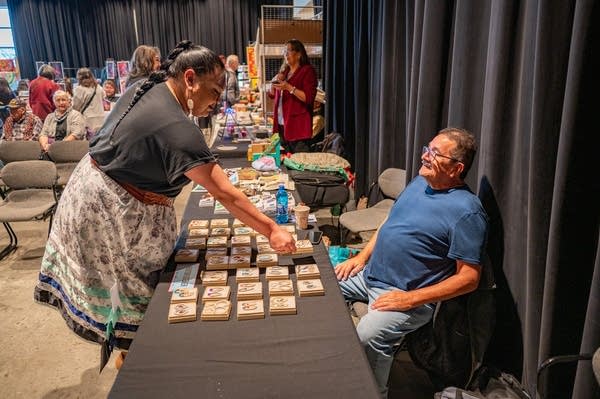 A man sits at a table as a woman looks over the items on sale.