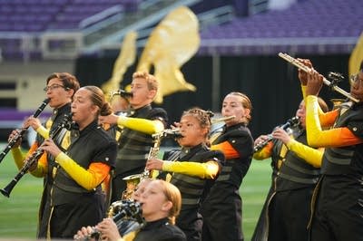 A marching band performs on the field of a football stadium.