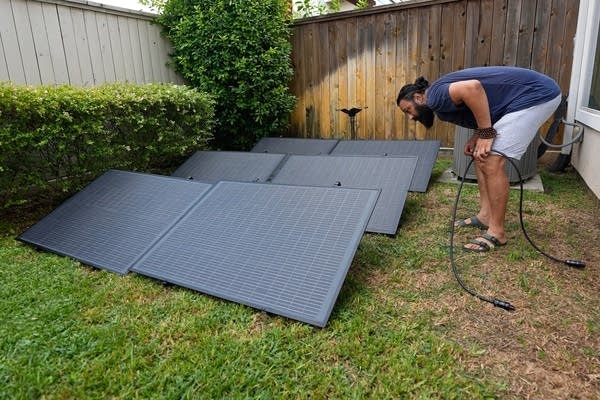 A man leans over to check solar panels he's installing in his yard.