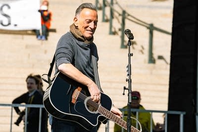 A man with a guitar interacts with fans from an outdoor stage at a large rally