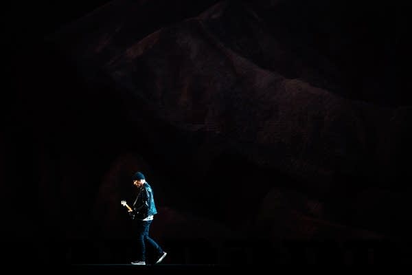 A man walks across a large stage playing guitar