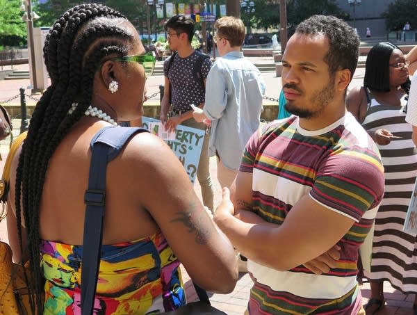 Jeremiah Ellison faces a woman with his arms crossed as they talk outside.