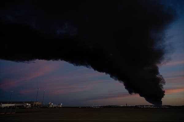 Smoke and flames rise from a plane crash at sunset.