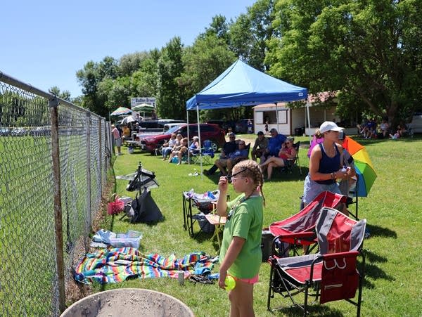 people stand and sit next to a chain link fence 
