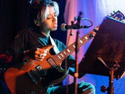 A woman sings into a microphone while holding a guitar